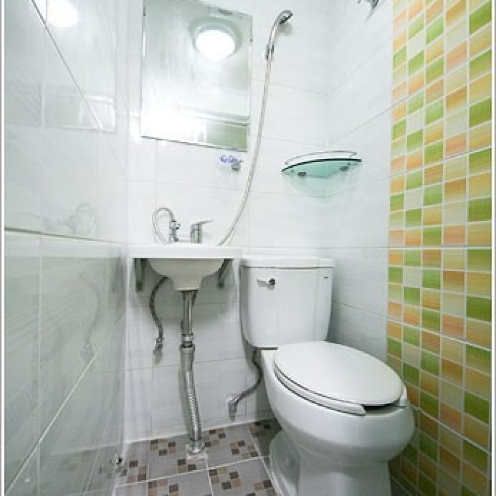 トイレとシャワーが設置されたバスルームの内部。白いタイルとカラフルなタイルの壁があり、鏡や洗面台も見える。