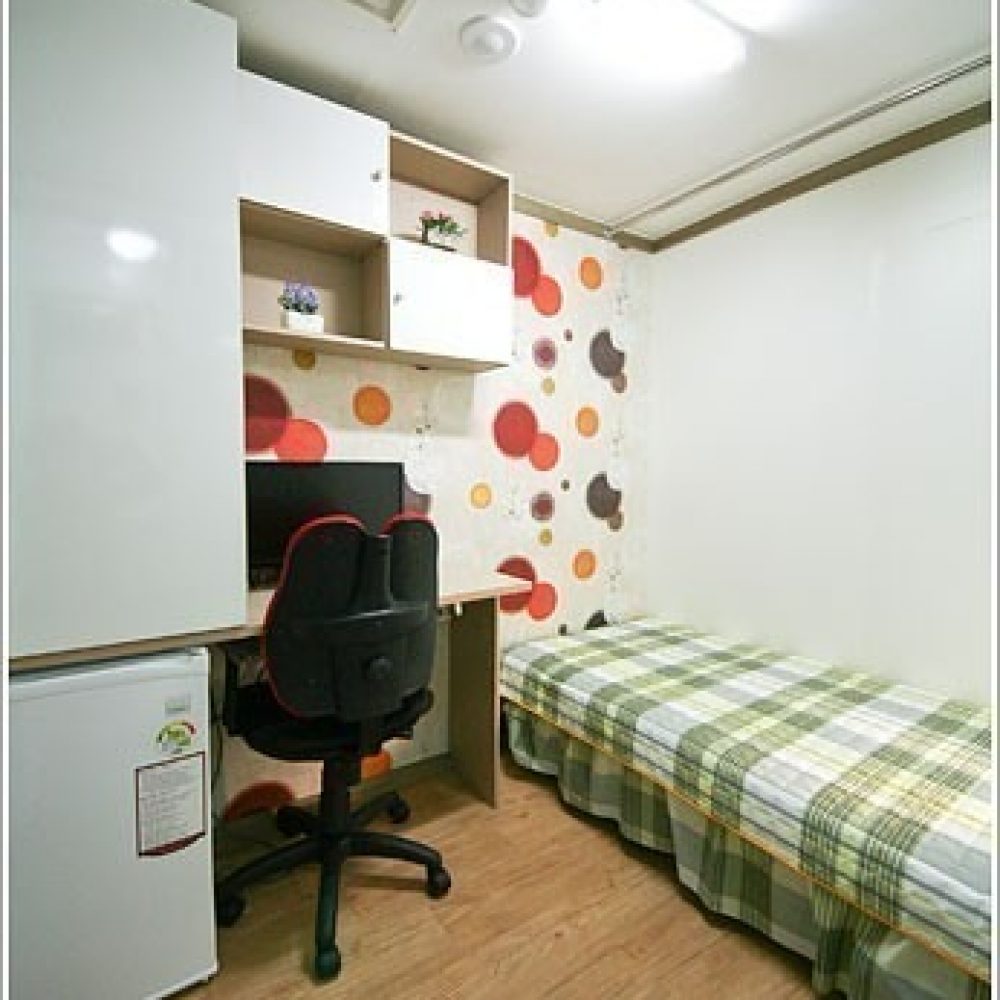 白い壁に赤い丸模様が散りばめられた部屋。 机と椅子、ベッドなどが配置されたシンプルな学生寮の部屋のイメージです。