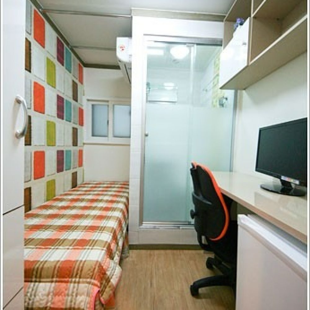 色とりどりの壁が印象的な部屋の画像です。部屋の中央にベッドが置かれ、その横にはデスクとチェアがあります。全体的にモダンな雰囲気の部屋ですね。