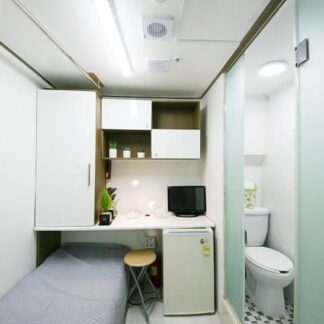 小さい部屋の中に必要な家具や設備がよく収まっている効率的な空間。テレビや冷蔵庫、収納棚など、狭い中にも生活に必要なものがきちんと配置されている。白と灰色を基調とした清潔感のある内装も印象的です。