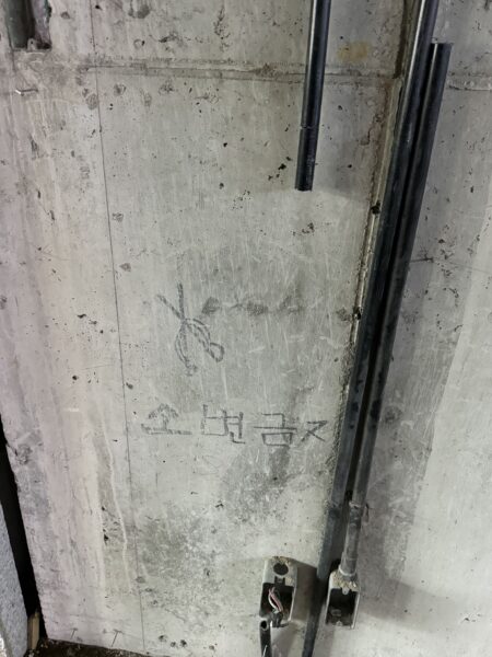 コンクリート壁に残された落書きと配線。展示空間の裏側や建築の痕跡がそのまま露出している。