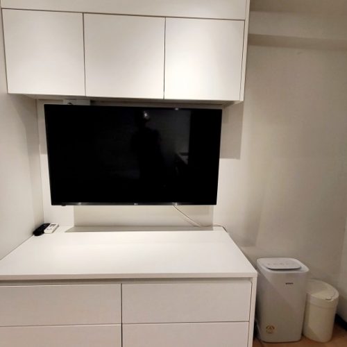画面に映っているのは白い家具に設置されたテレビです。テレビの下には家電製品が置かれています。部屋の雰囲気は落ち着いた感じで、モダンな印象を受けます。