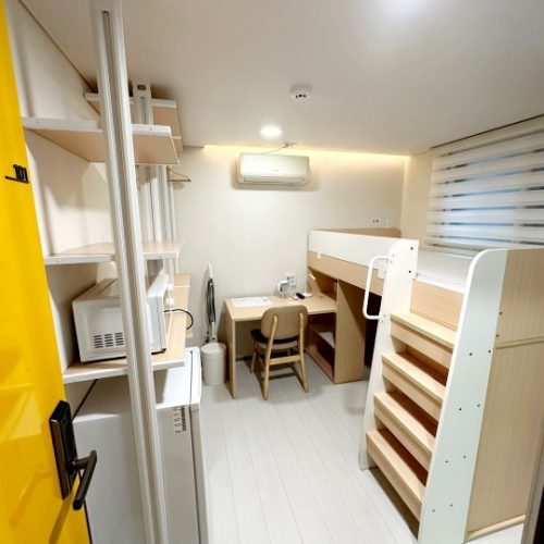 画像は白と黄色のカラーリングのきれいな部屋を示しています。部屋には扉、棚、机、椅子などの家具が配置されています。室内は清潔で整理されており、居心地の良い雰囲気を感じさせます。