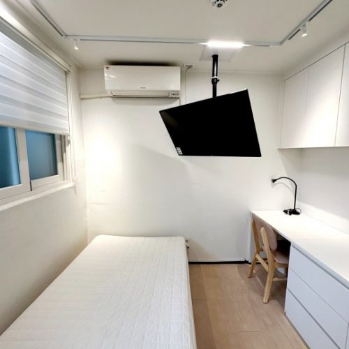 天井に掛けられたプロジェクターと、ベッドとデスクが置かれた居心地のよい部屋の写真です。