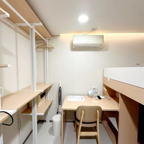 このイメージは明るい部屋で、棚や机、エアコンなどの家具が配置されています。部屋全体がきれいに整理されており、落ち着いた雰囲気を感じられます。