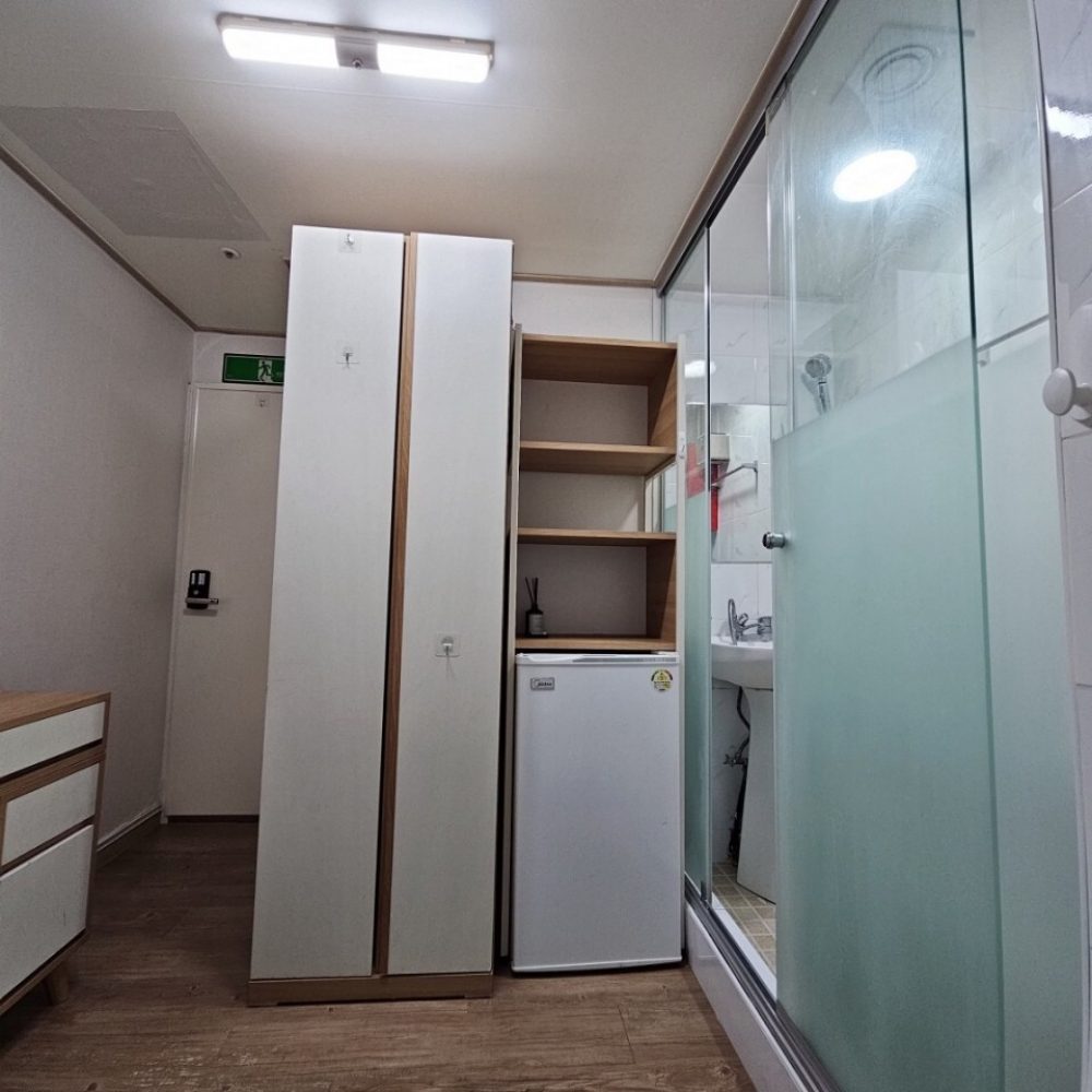 この画像は、小さな部屋の内部を写したものです。部屋の中には、冷蔵庫、収納棚、ガラス製のドアがあります。床はうたかたの木材で、明るい雰囲気の部屋になっています。全体的にシンプルで機能的な作りになっていますね。