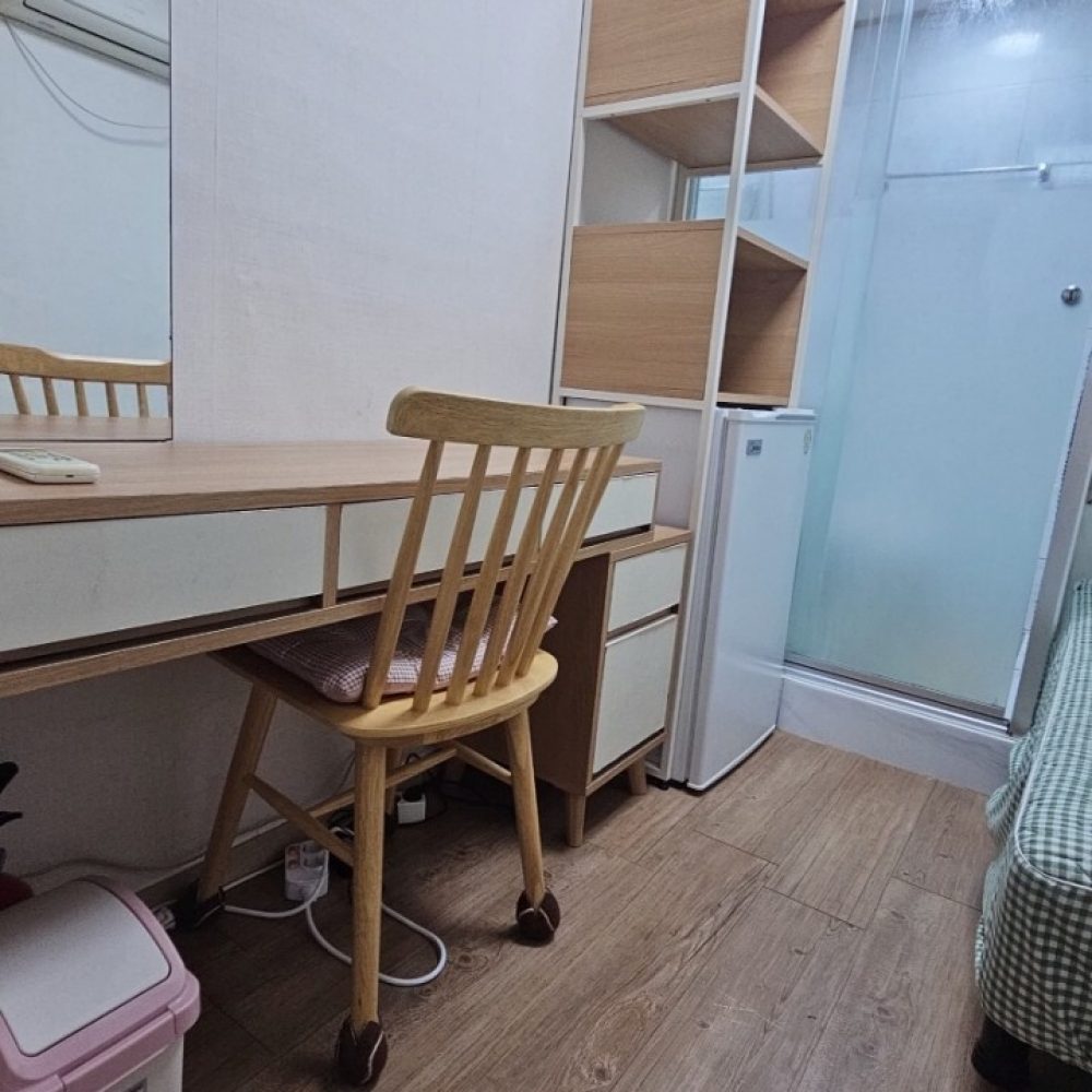 部屋の中には、机と椅子が置かれています。机の上には、コンピューターやその他の物品が置かれています。部屋の奥には、棚やタンスなどの収納家具が設置されています。部屋全体が明るく、清潔な印象を受けます。